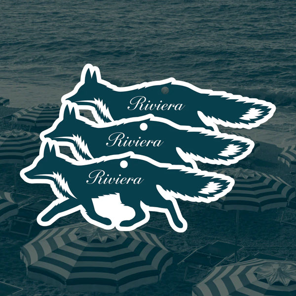 Three blue and white fox-shaped car air fresheners on a blue background with the word "Riviera" on them in a cursive font