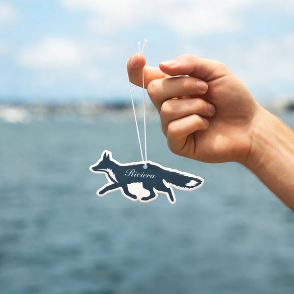 Person holding "Riviera" air freshener by Guy Fox