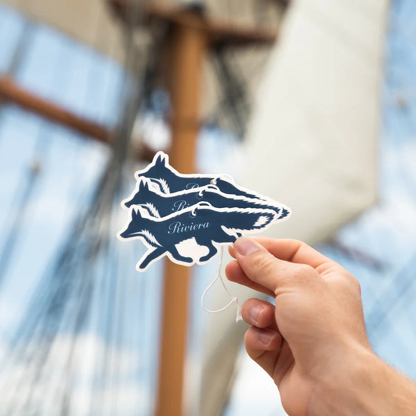 Person holding three Guy Fox "Riviera" fox -shaped air fresheners against a blurred background of a sailing ship