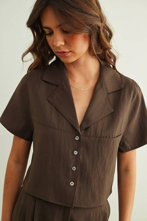 Woman wearing a brown short-sleeve blouse with buttons on a plain background