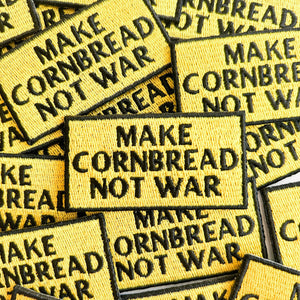 Yellow patches with 'MAKE CORNBREAD NOT WAR' in black block text on a pile.