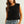 Woman wearing a black sleeveless knitted top and blue jeans against a plain background